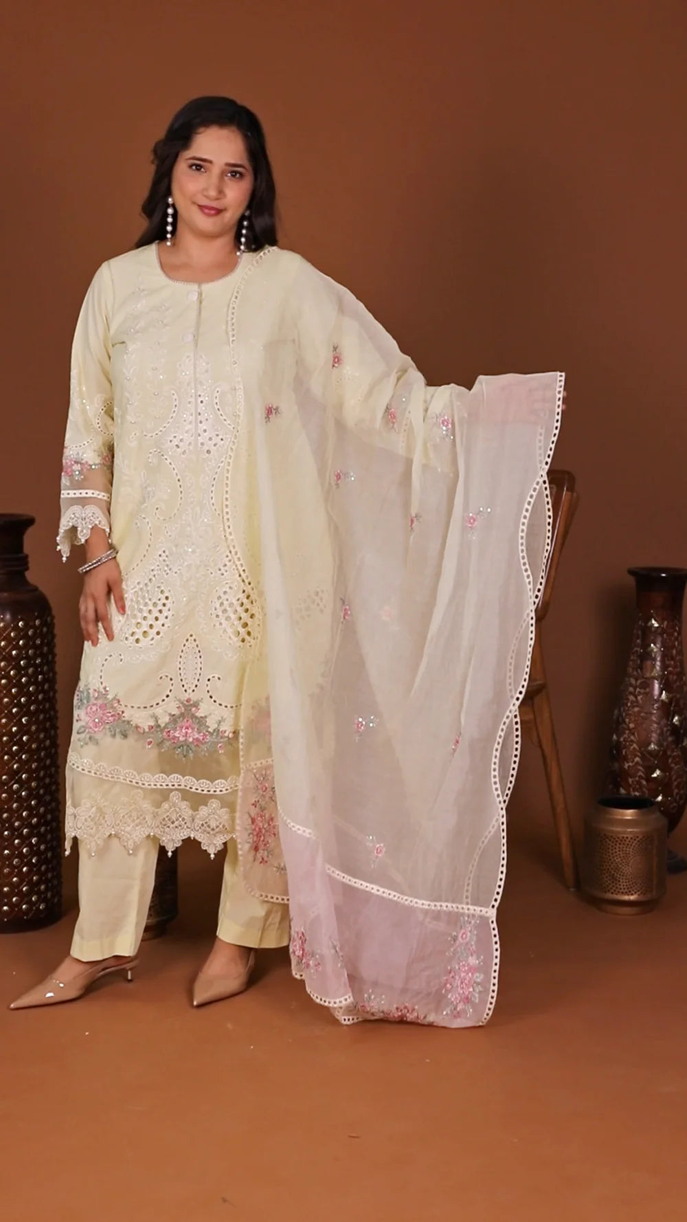 Woman wearing a cream-colored traditional outfit with floral patterns on a brown background